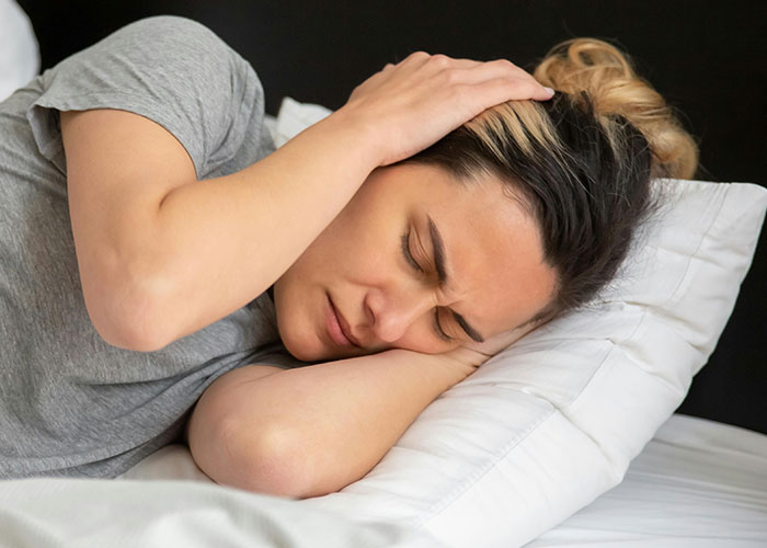 Woman lying on bed holding head in discomfort, illustrating one of the 51 life hacks people discovered accidentally and still use.