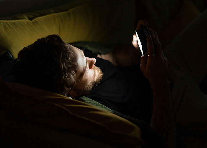 Man lying on couch at night, staring at phone screen, reflecting creepy things women said that left men horrified.