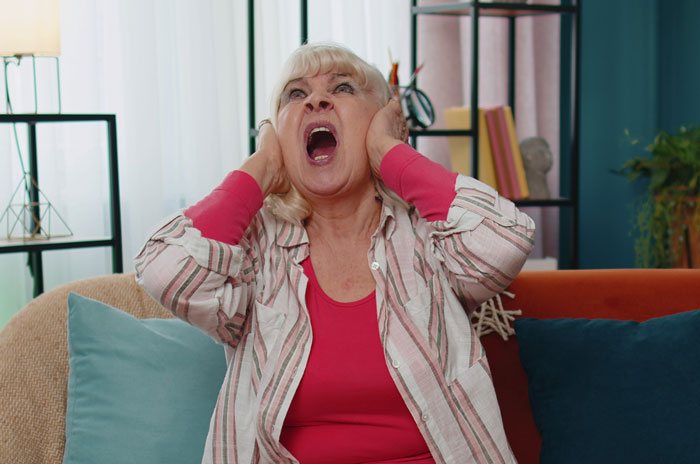 Angry older woman covering ears and yelling on couch, illustrating unhinged behavior during new mom confrontation with MIL.