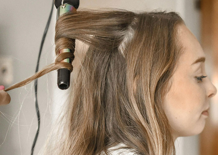 Woman having her hair curled with a curling iron, illustrating cosmetic procedure preparation and beauty treatment concerns.