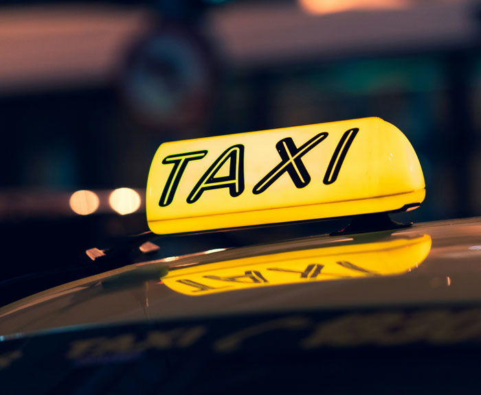 Illuminated taxi roof sign at night with reflection, suggesting urban travel in worst places.