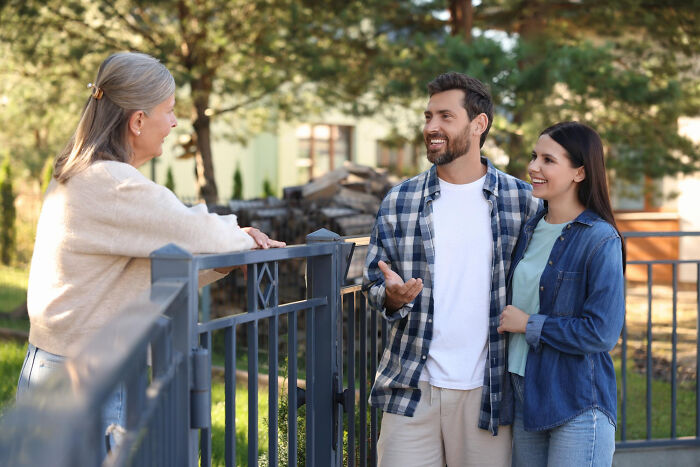 A couple talking to a neighbor at the fence, sharing moving advice and zip-line your boxes out tips outdoors.