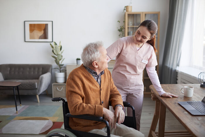 A caregiver smiling and talking with an elderly patient with dementia in a cozy living room setting.