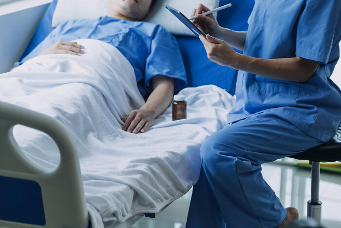 Nurse in blue scrubs taking notes beside a patient in hospital bed, setting for scary ghost stories hospital work.