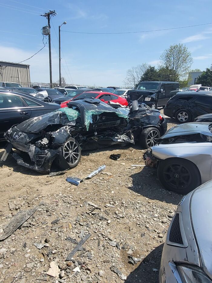 Severely wrecked black car in a lot, illustrating nightmare situations people survived against all odds.