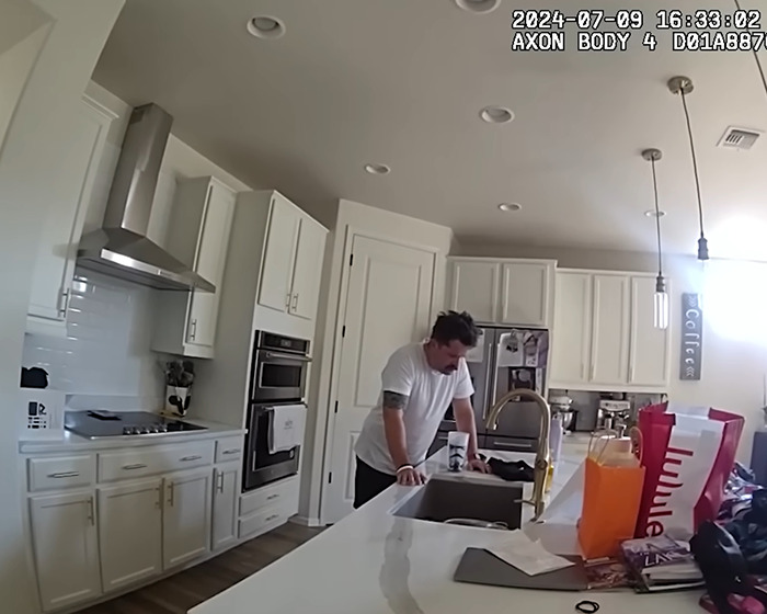 Man in white shirt standing in kitchen, leaning on counter, related to dad watched adult videos hot car incident.