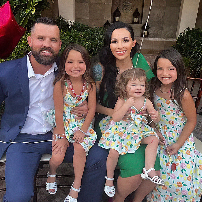 Family portrait with smiling parents and three daughters wearing matching floral dresses on a sunny day outdoors
