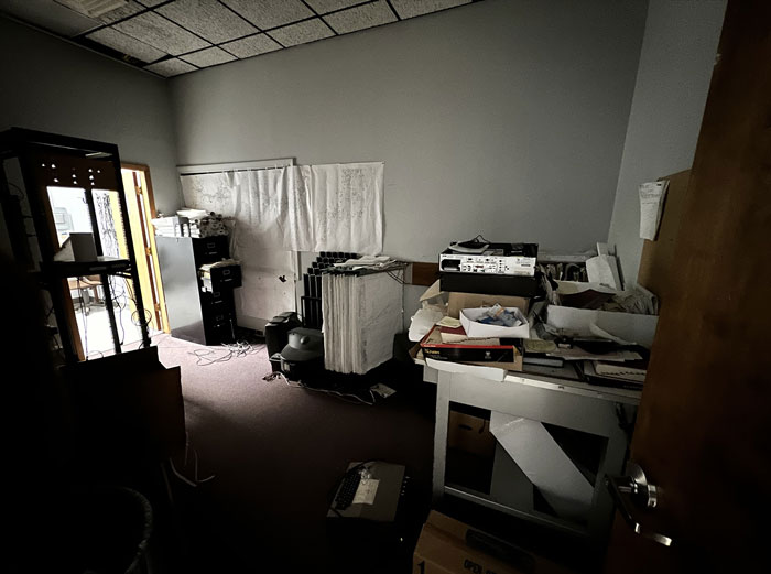 Cluttered office space covered in dust and grime with scattered papers and old equipment in a neglected workplace environment