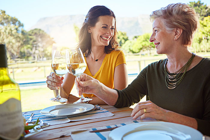 Two women smiling and toasting with white wine outdoors during a heartfelt conversation about family. Two women smiling and toasting with white wine outdoors during a heartfelt conversation about family.