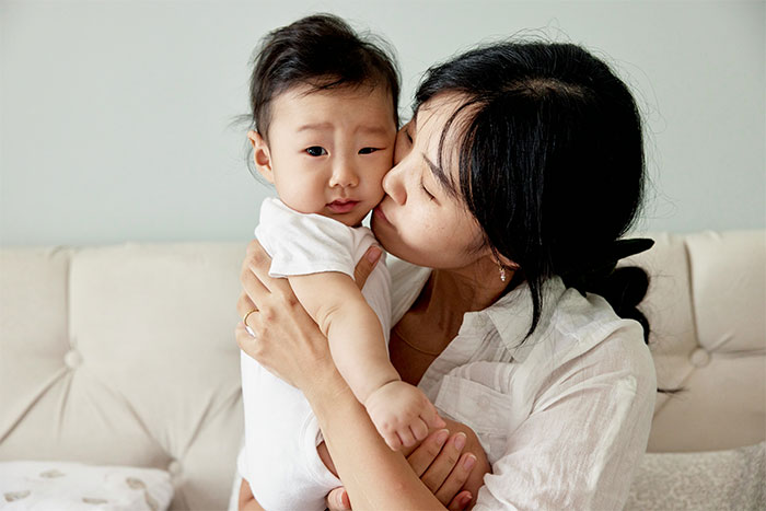 Woman holding and kissing her baby, illustrating concern about unvaccinated kids in social settings.