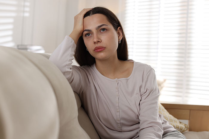 Woman looking upset and contemplative on couch, reflecting on feelings related to being an ugly woman.
