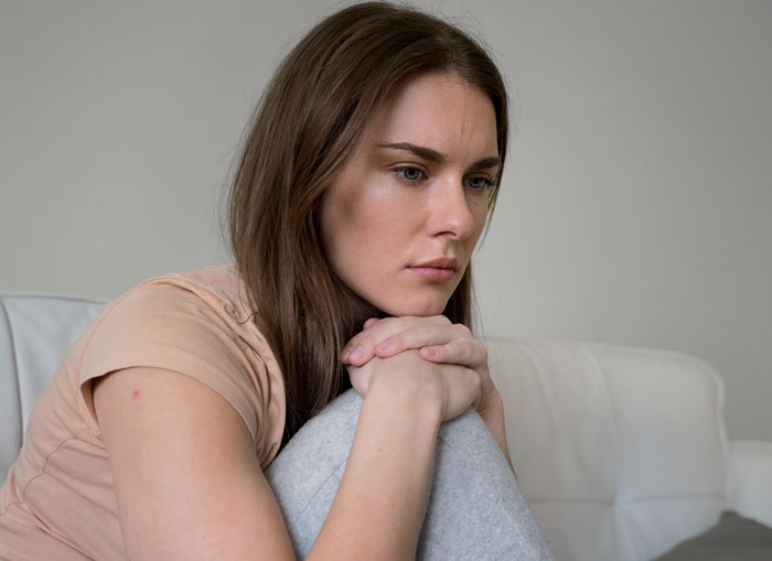 Woman sitting on couch looking sad and contemplative, reflecting on challenges of having a deaf baby and family strain.