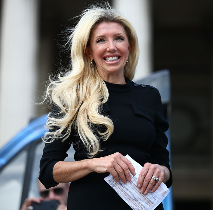 Woman with long blonde hair holding papers, smiling outdoors, related to coroner exposing mom influencing refusal of chemo. Woman with long blonde hair holding papers, smiling outdoors, related to coroner exposing mom influencing refusal of chemo.
