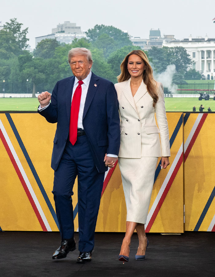 Melania Trump and Donald Trump walking hand in hand outdoors with White House in the background.