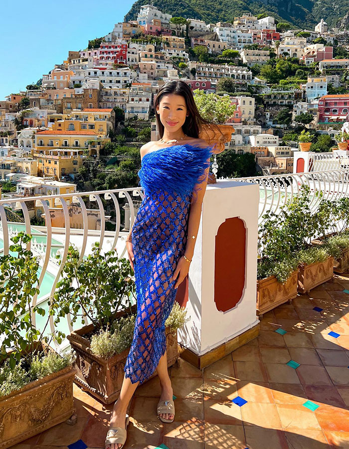 Billionaire influencer posing in a blue dress on a balcony with luxury Hermès shopping haul backdrop. Billionaire influencer posing in a blue dress on a balcony with luxury Hermès shopping haul backdrop.