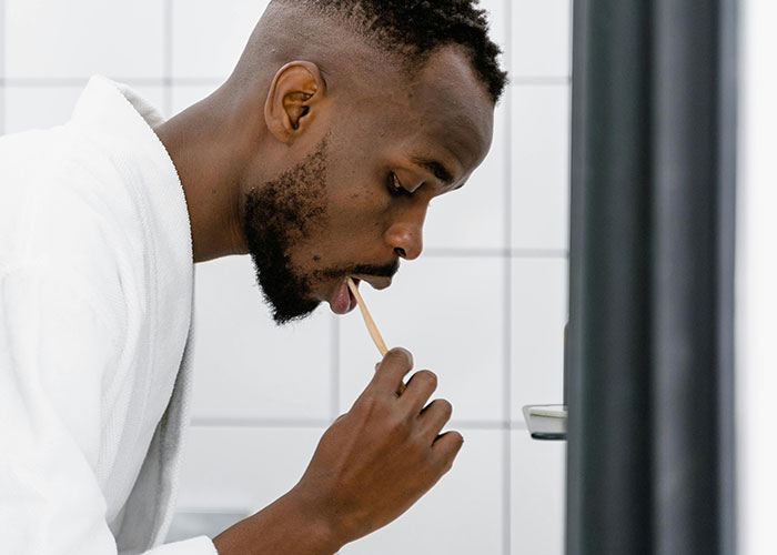 Man in a white robe using a bamboo toothbrush in a modern tiled bathroom, demonstrating simple life hacks for daily routine.