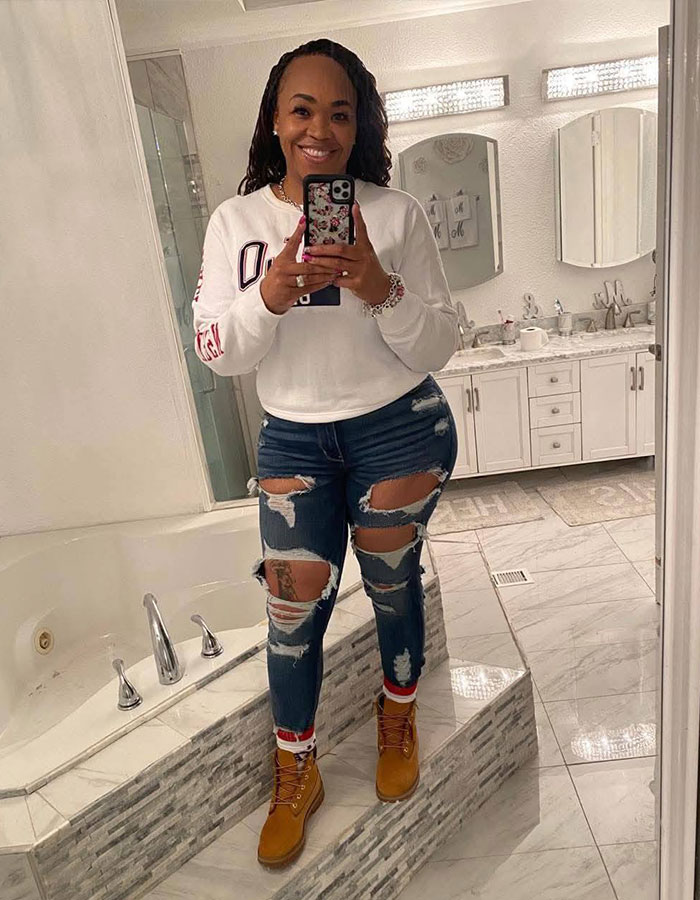 Woman taking mirror selfie in bathroom, wearing ripped jeans and boots, related to unhinged act breaking into boyfriend&rsquo;s home.