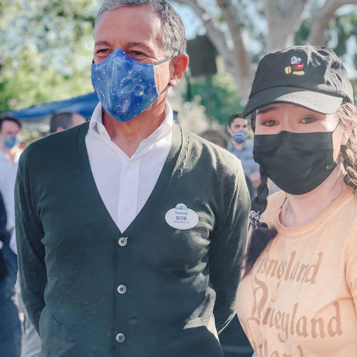 Man and woman wearing face masks at an outdoor event, woman wearing a Disney-themed hat and shirt, Disney superfan context.