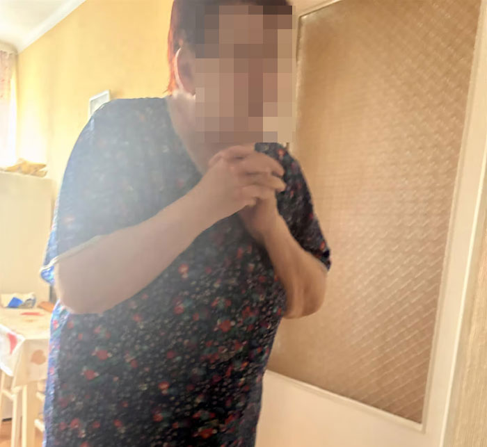 Woman in floral dress standing indoors, appearing concerned after being missing and found emaciated for 27 years.