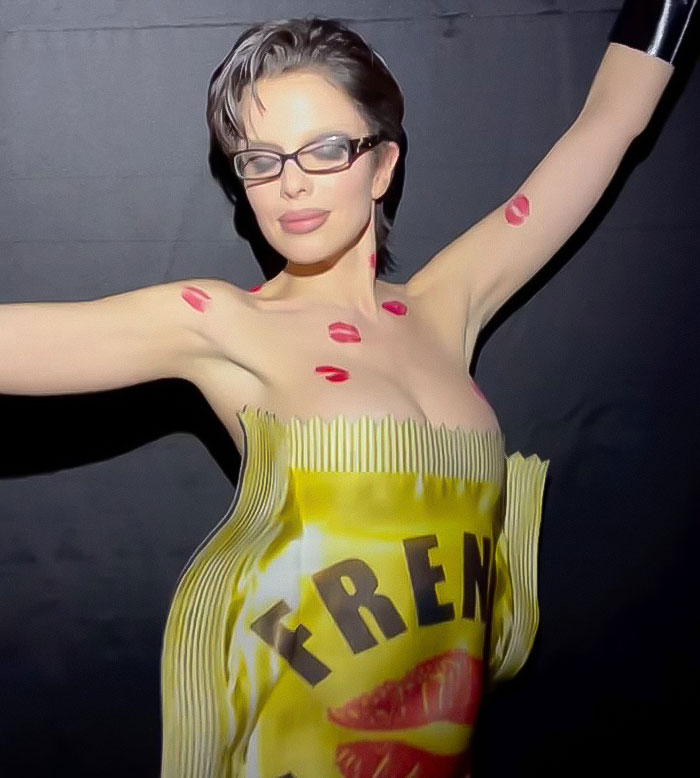 Julia Fox wearing a barely-there dress with lip print designs, posing confidently at a gala event with arms raised.