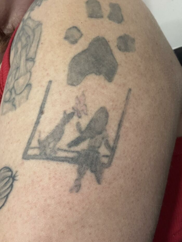 Tattoo of a girl and a dog on a swing with a paw print above on a person's upper arm among other tattoos.