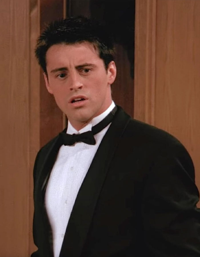 Matt LeBlanc as Joey in a black tuxedo, looking surprised in a wood-paneled room in unaired episodes.
