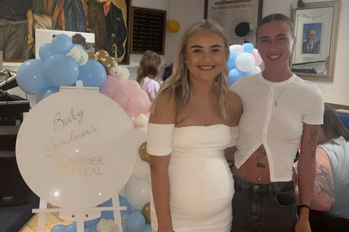 Two women smiling at a gender reveal party with balloons, related to woman's outrageous 10-month lie unraveling.