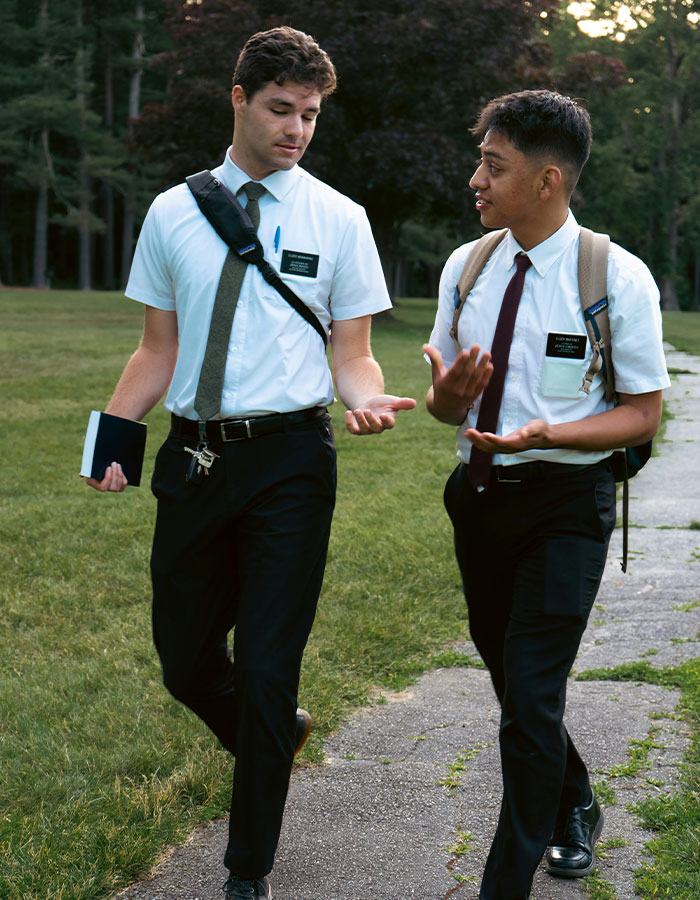 Two young men in white shirts and ties walking outdoors, discussing the Mormon Backflip Theory trend.