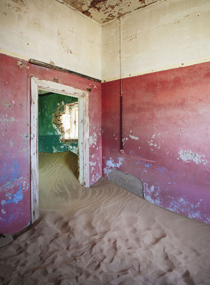 Desert sand filling abandoned home with peeling red and green walls in a surreal sand castle scene.