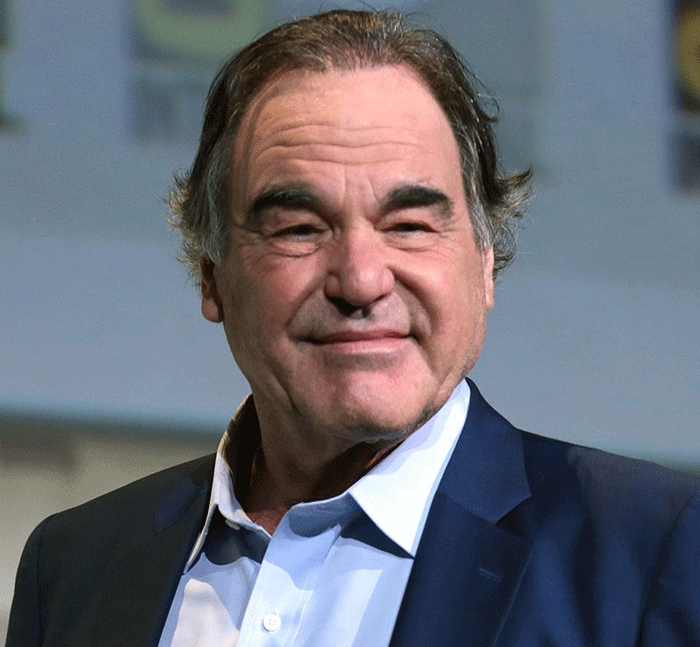 Man in blue suit and light blue shirt smiling subtly during an indoor event discussing Emilio Estevez Charlie Sheen Tom Cruise news. Man in blue suit and light blue shirt smiling subtly during an indoor event discussing Emilio Estevez Charlie Sheen Tom Cruise news.