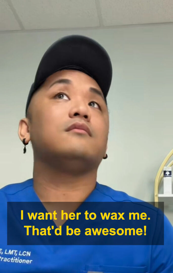 Man in blue uniform and black cap looking up during aesthetician interaction about waxing appointment.