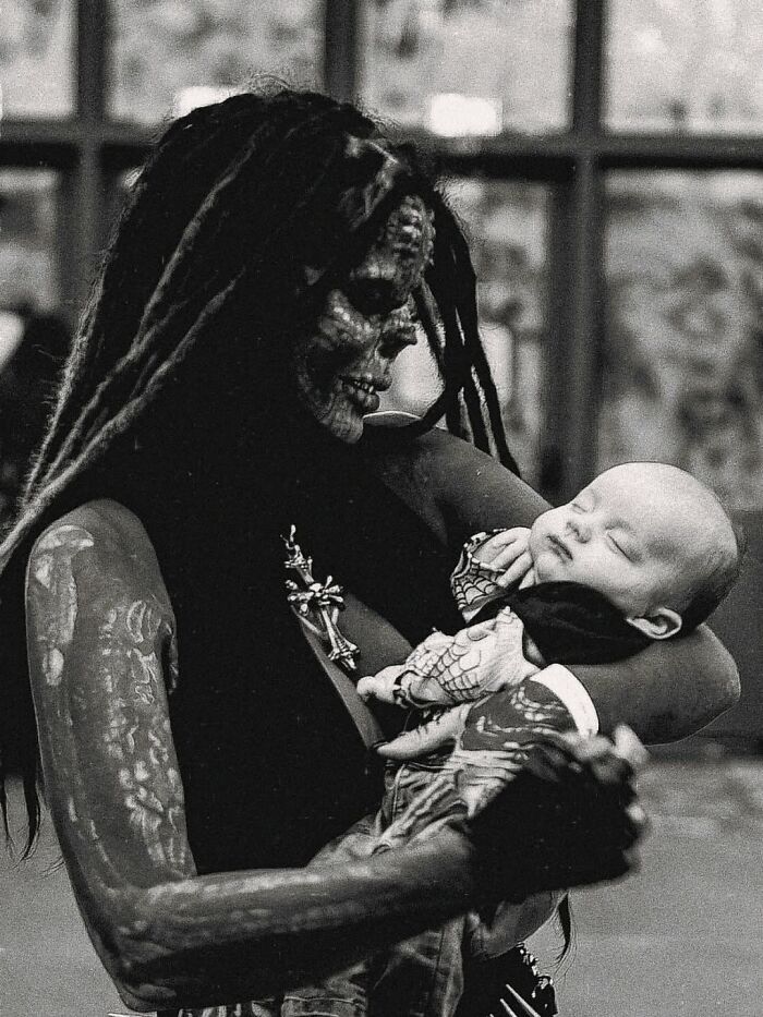 Tattooed woman with skeletal face paint holding a sleeping baby, highlighting before-and-after photos viral story.