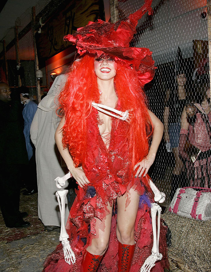 Heidi Klum in a nightmare-level Halloween costume with bright red hair and skeletal accessories at a festive event.