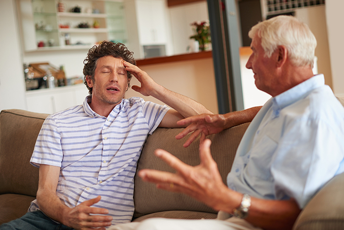 Two men having a tense conversation on a couch, highlighting family conflict over caring for disabled sister. Two men having a tense conversation on a couch, highlighting family conflict over caring for disabled sister.