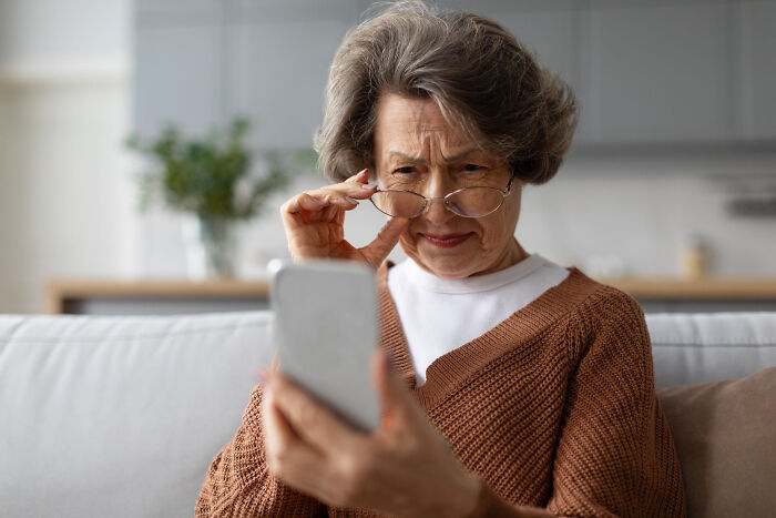 Elderly woman struggling with smartphone, showing parents' technology skills in a funny and relatable moment at home.