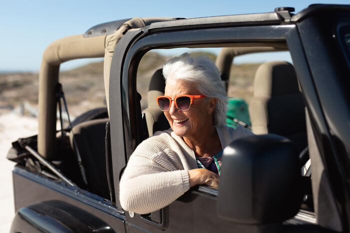Older woman wearing sunglasses smiling while sitting in a jeep.