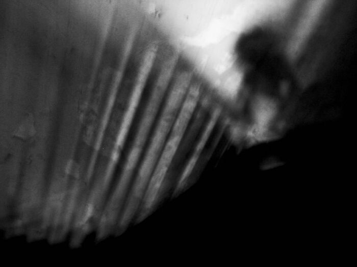 Blurry black and white photo with an eerie shadow resembling a figure next to a vertical striped surface, creepy photo moment.