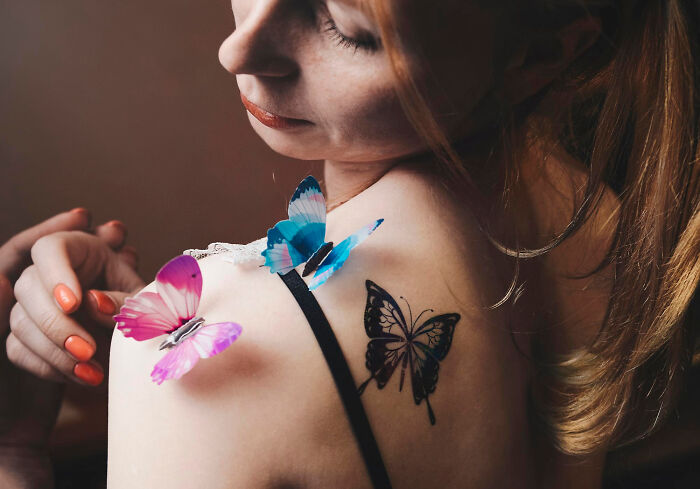Young woman with butterfly tattoo and colorful butterflies on shoulder, capturing a calm and reflective moment.