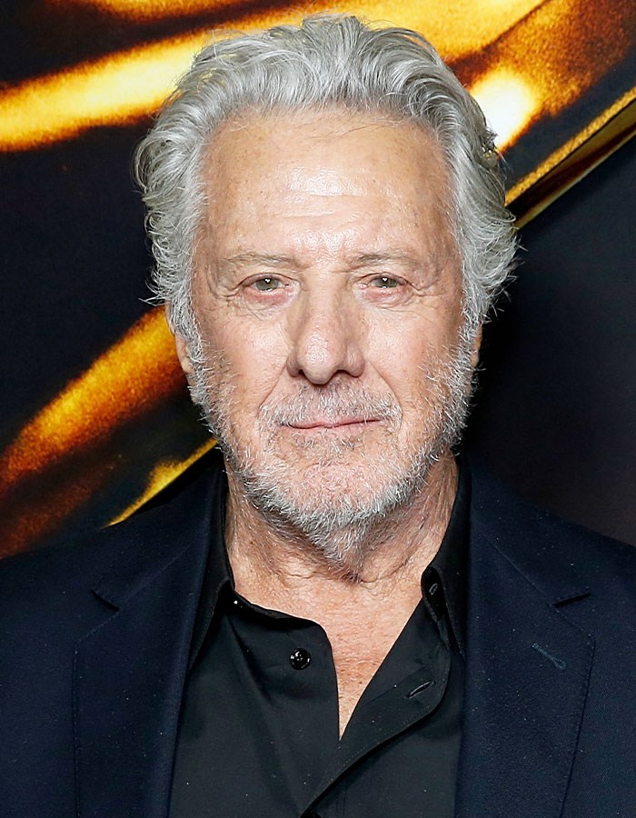 Older man with gray hair and beard wearing a black shirt and jacket at an event featuring famous men shorter than imagined.