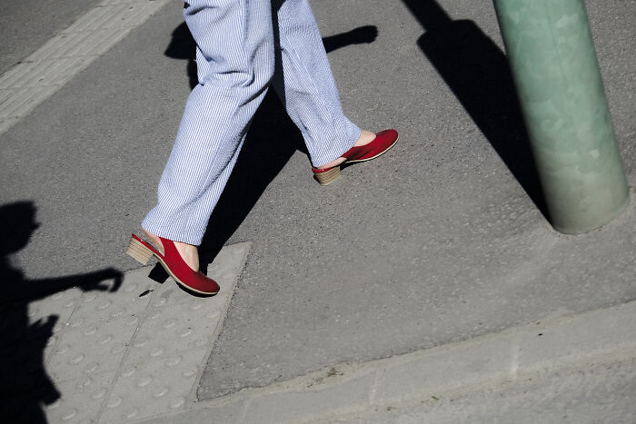 Person walking on city sidewalk wearing red shoes and striped pants in a stunning street photography shot capturing life’s moments.