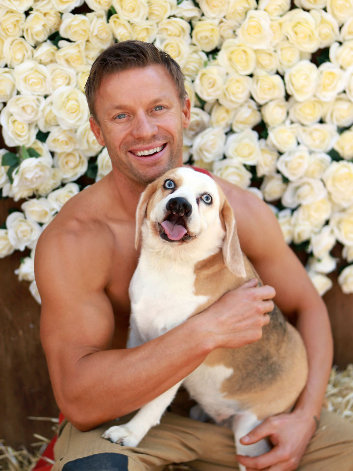Smiling firefighter holding an adorable dog with blue eyes in front of a white rose flower wall for Australian calendar.