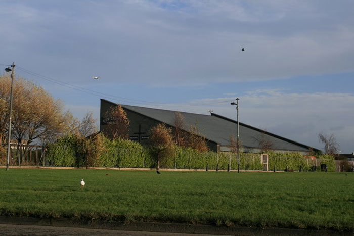 Empty grassy park with lone bird and low industrial building under gray sky, illustrating worst places