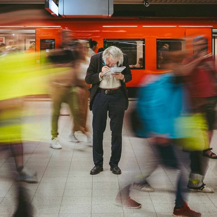 Elderly man reading a book in a busy subway station, capturing the beauty and wisdom of old age in a street photo.