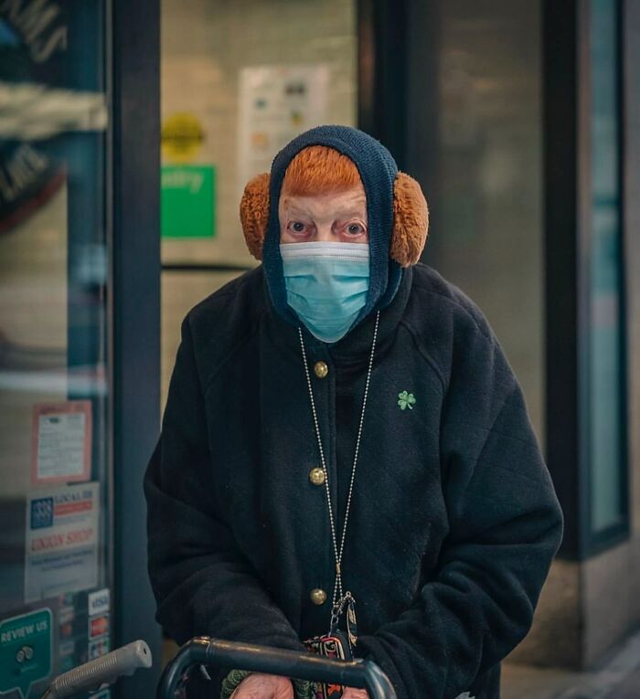 Elderly person wearing face mask and earmuffs, using a walker in a street setting capturing the beauty and wisdom of old age.
