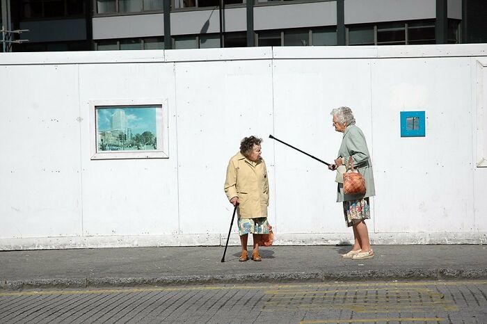 Two elderly women in conversation on a city sidewalk, capturing the beauty and wisdom of old age in street photos.