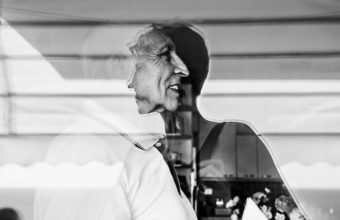 Elderly man with reflection in window, capturing the beauty and wisdom of old age in a street photo.