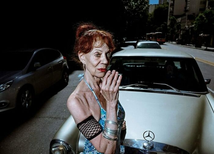 Elderly woman with red hair and bracelets standing confidently in street photo capturing beauty and wisdom of old age.