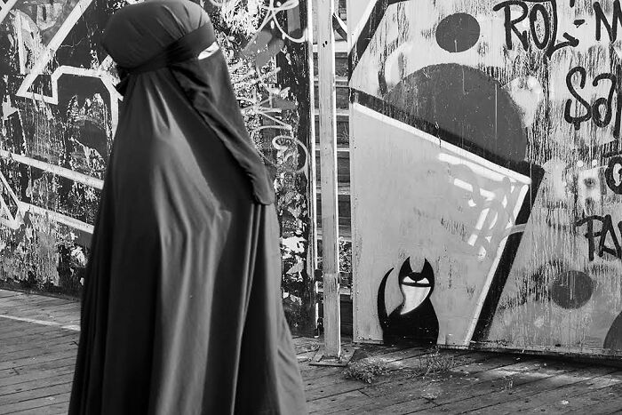 Woman in traditional attire walking past graffiti art of a cat on Istanbul streets capturing life and cats stealing the show.