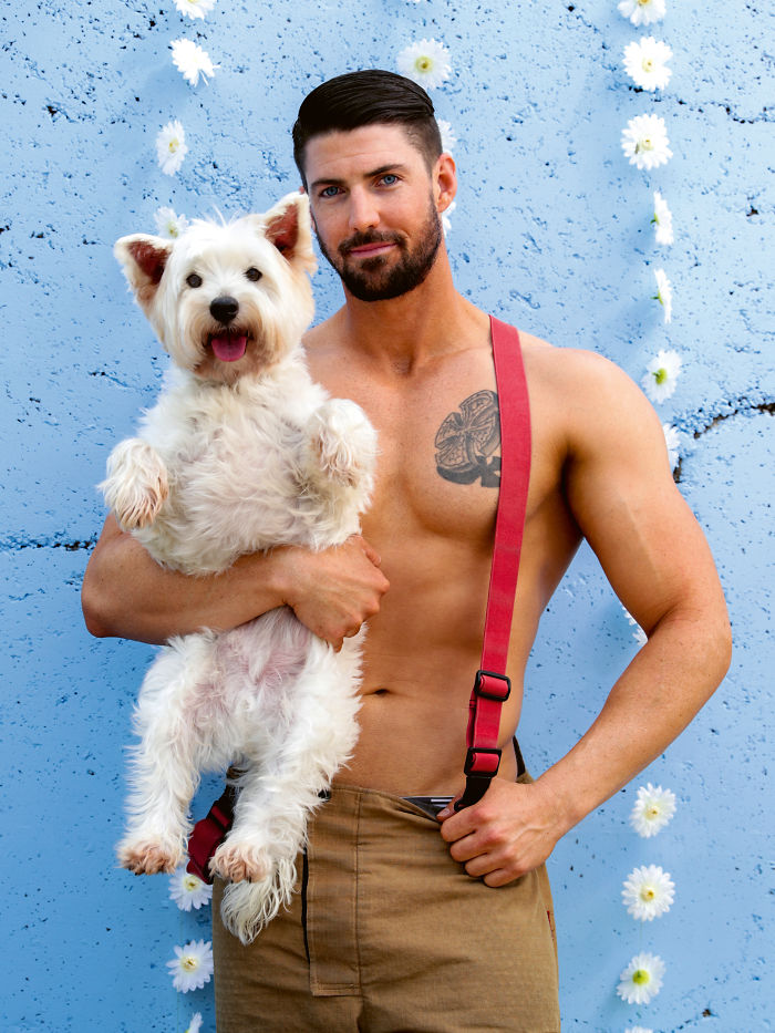 Shirtless firefighter holding a fluffy white dog with a blue floral background from Australian calendar photos.