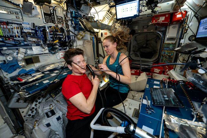 Two astronauts floating inside a spacecraft surrounded by equipment in an epic astronomy photos setting.
